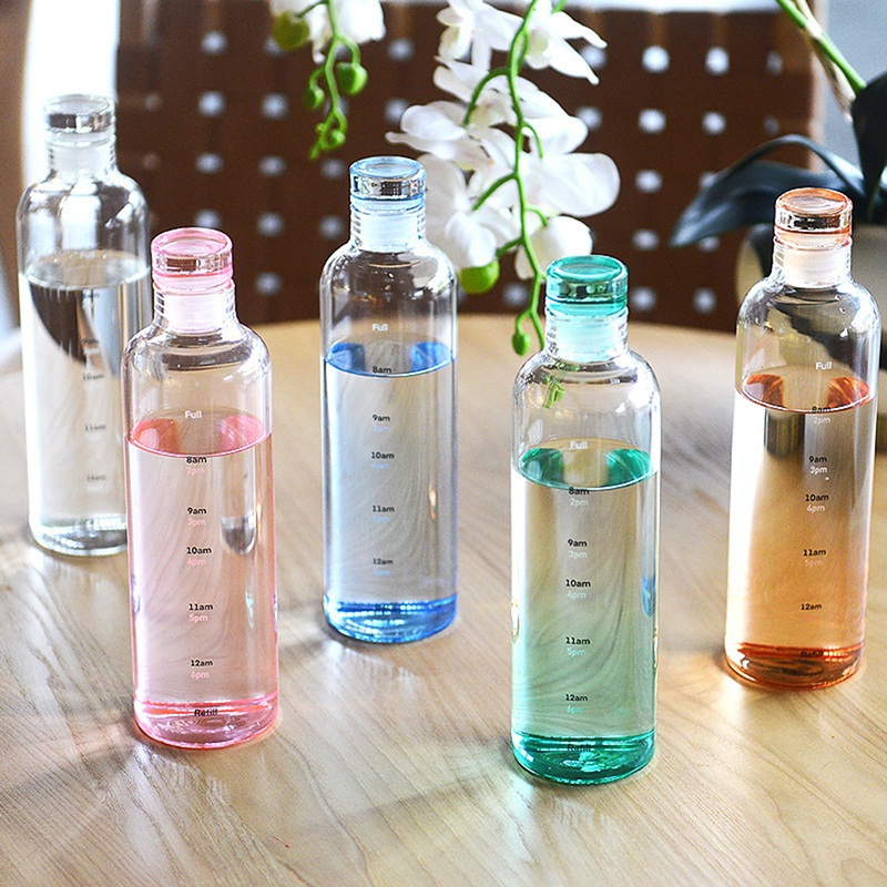 Five transparent bottles with colored caps on a wooden surface, with flowers in the background.