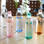 Five transparent bottles with colored caps on a wooden surface, with flowers in the background.