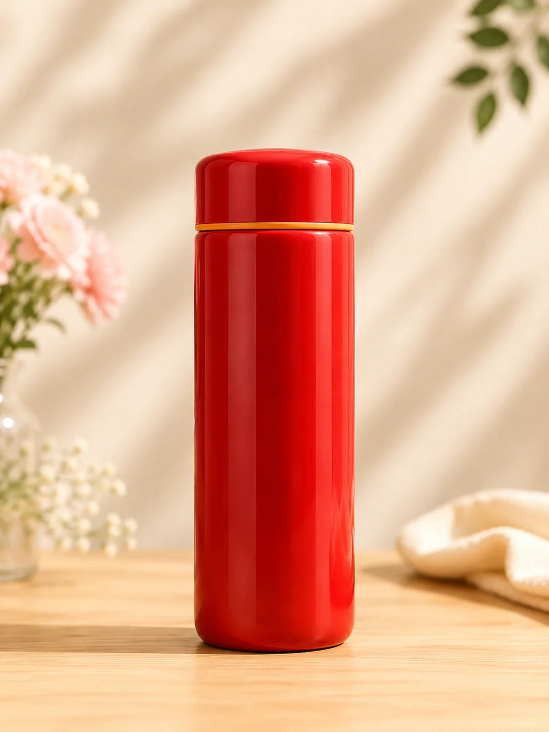 Red thermos bottle on a wooden surface with a blurred floral background