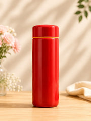 Red thermos bottle on a wooden surface with a blurred floral background