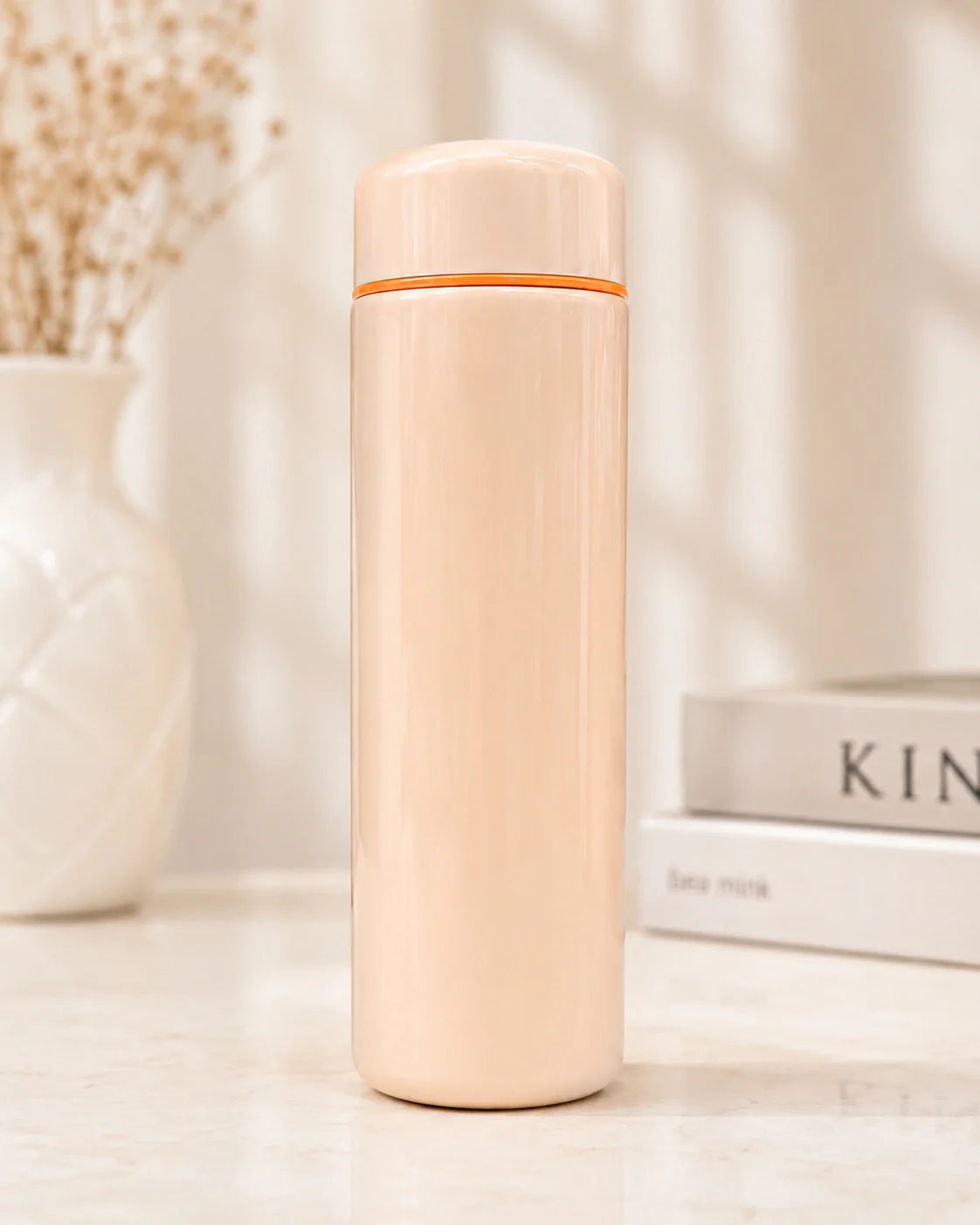 Beige thermos bottle with orange top on a light surface