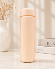 Beige thermos bottle with orange top on a light surface