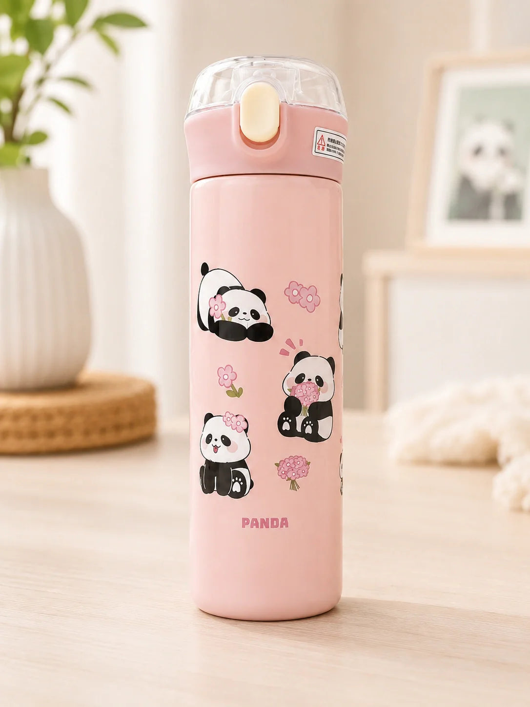 Pink thermos bottle with panda designs on a light wooden surface.
