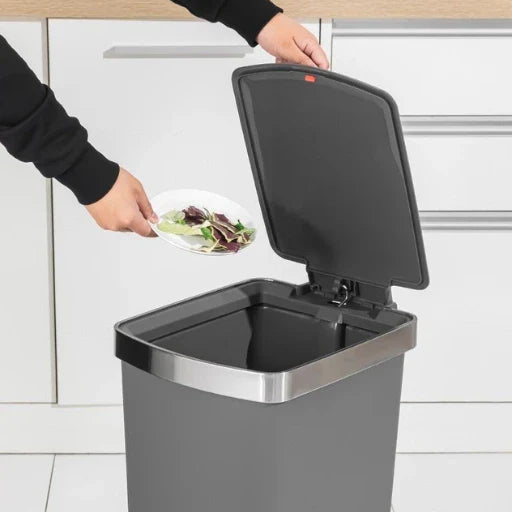 Person disposing of food waste into a kitchen compost bin.