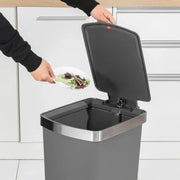 Person disposing of food waste into a kitchen compost bin.
